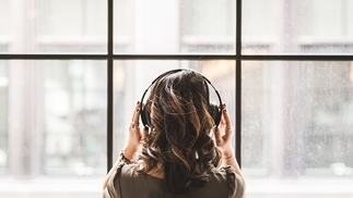 Woman with long brown hair looking out a rain-covered window with headphones on