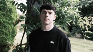 Photo of Irish DJ Dylan Fogarty wearing a black jumper in front of a green leafy garden