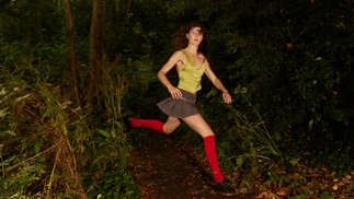 Photo of Clarissa Connelly wearing red long socks and a green shirt while running through the woods