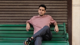 Photo of DJ and producer FILM sitting on a green bench wearing a pink shirt