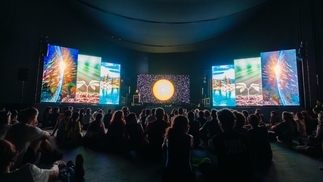 A series of colourful screens in a dark room with music fans watching