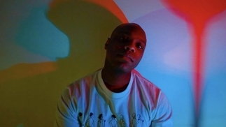 Photo of Kellen303 wearing a white t-shirt in front of a rainbow projector light