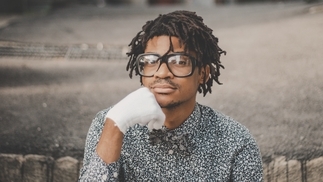 Photo of omniboi posing while wearing a patterned shirt and white glove