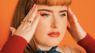 Photo of Scarlett O’Malley wearing red lipstick and a blue bandana on an orange background