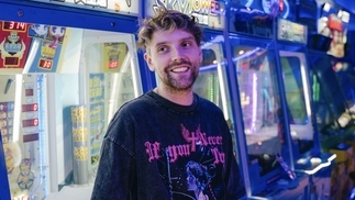 Photo of Faint Rings smiling and wearing a black tee in an arcade