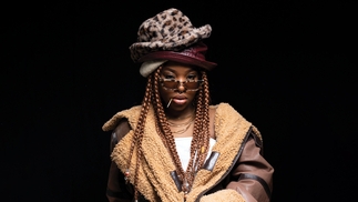 Photo of Meduulla wearing a brown fur coat and an array of hats