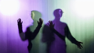 The Chemical Brothers press shot, showing the pair blurred behind a see-through panel, in purple and green light. A silhouette of hands against the surface is in front of them