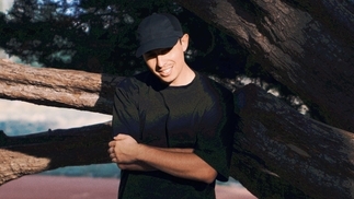 Photo of Gipsyan wearing a black t-shirt in front of a tree and sunset