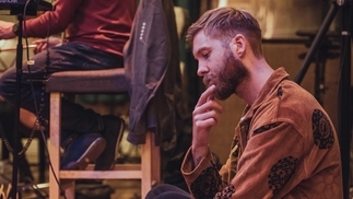 Photo of Calvin Harris sitting on the floor in a studio wearing a brown shirt