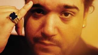 Photo of Toribio in a soft, orange focused light. His right pinky has a black and gold ring on it and he is holding it against his eyebrow