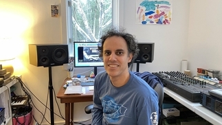 Four Tet sitting in his home studio, smiling at the camera