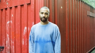 Photo of Christian AB standing in front of a red shipping container wearing a blue shirt