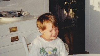 Childhood photo of HNNY grimacing and sitting at a kitchen table