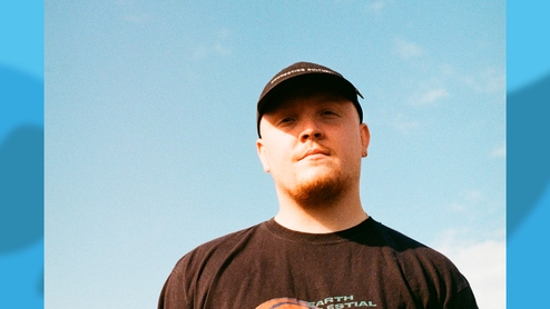 Chris Stussy in a black t-shirt and hat against a blue sky