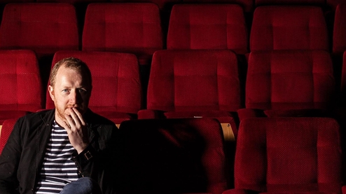 Phil Kieran sitting in a cinema filled with red seats