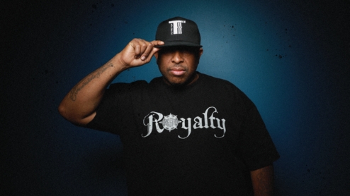 Press shot of DJ Premier in a black hat looking toward the camera in a t tshirt that says "Royalty"