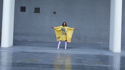 Honey Dijon poses in a yellow banner dress in an industrial setting