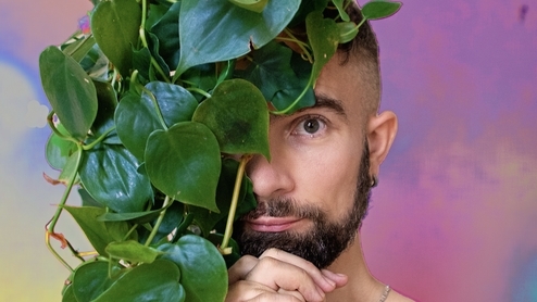 Photo of Olof Dreijer peering out from behind a vine of leaves with a pink sunset background