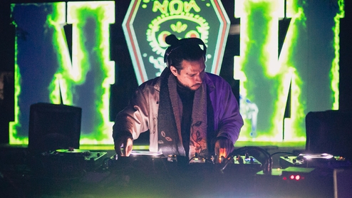 Photo of Sonido Berzerk DJing front of a green psychedelic light display