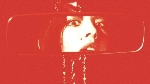 Red photo of Caroline Polachek looking into a car mirror 