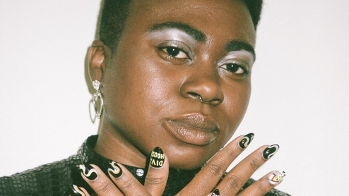 Photo of Dee Diggs holding up her colourful nails and wearing white eyeshadow