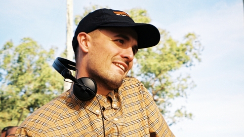 Ewan McVicar DJing outdoors at a festival in a cheque shirt