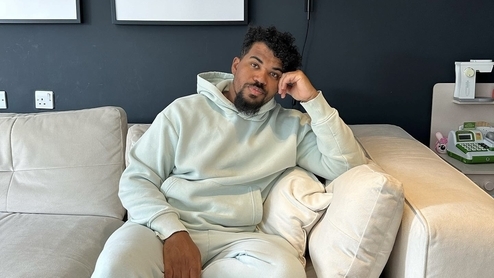 Photo of DJ Cuddles wearing a light blue tracksuit and sitting on a cream couch