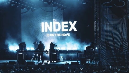 Photo of a blue-lit stage with the words ‘Index is on the move’ printed