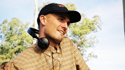 Photo of Ewan McVicar wearing a black hat and yellow shirt with headphones around his neck