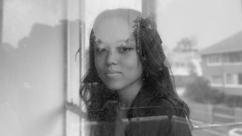 Black and white photo of Gonubie smiling and looking through a window with reflections