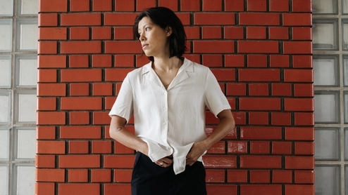 Photo of Monki wearing a white shirt and black trousers against a faux brick wall