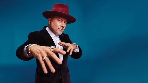 Photo of Louie Vega wearing a suit and red hat against a blue background
