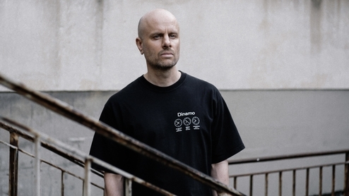 Photo of Kuttin Edge wearing a black t-shirt and standing on a grey industrial staircase