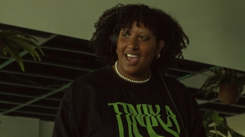 Photo of Tinika wearing a black and green shirt with her name on against a green background