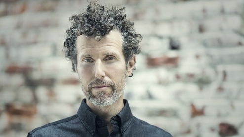 Photo of Josh Wink wearing a grey shirt in front of a brick wall