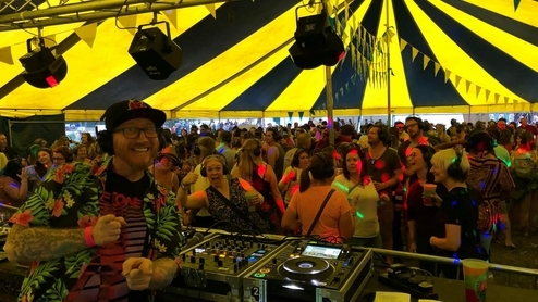 DJ PressPlay smiling at the camera while DJing in a festival tent