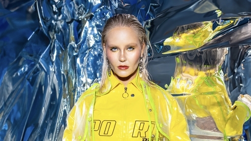 Photo of LUMI wearing a yellow cropped rain jacket in a reflective blue room