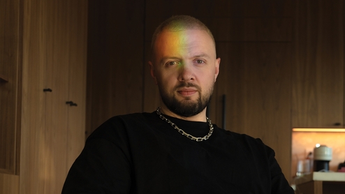 Photo of Chris Lake wearing a black t-shirt with a rainbow reflected on his face