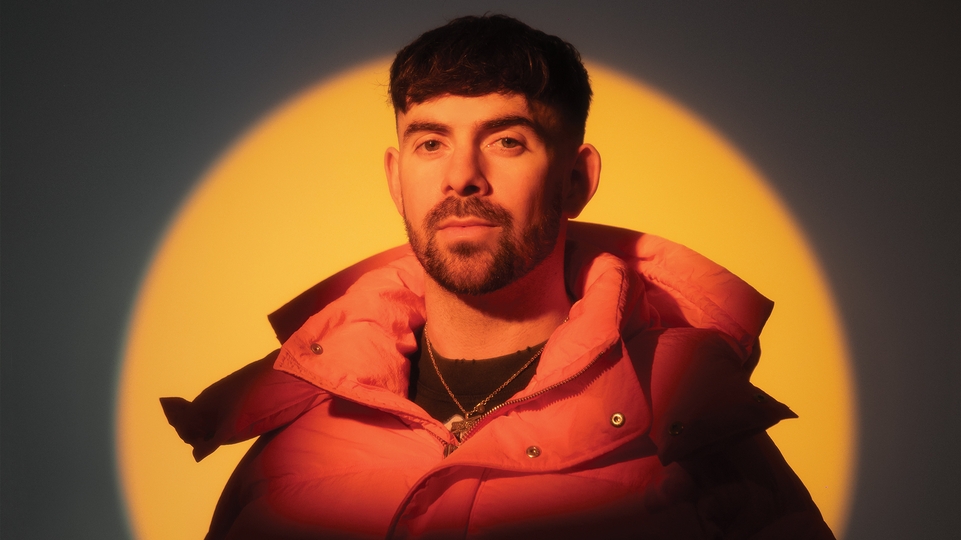 Patrick Topping in an orange coat lit up by a yellow light