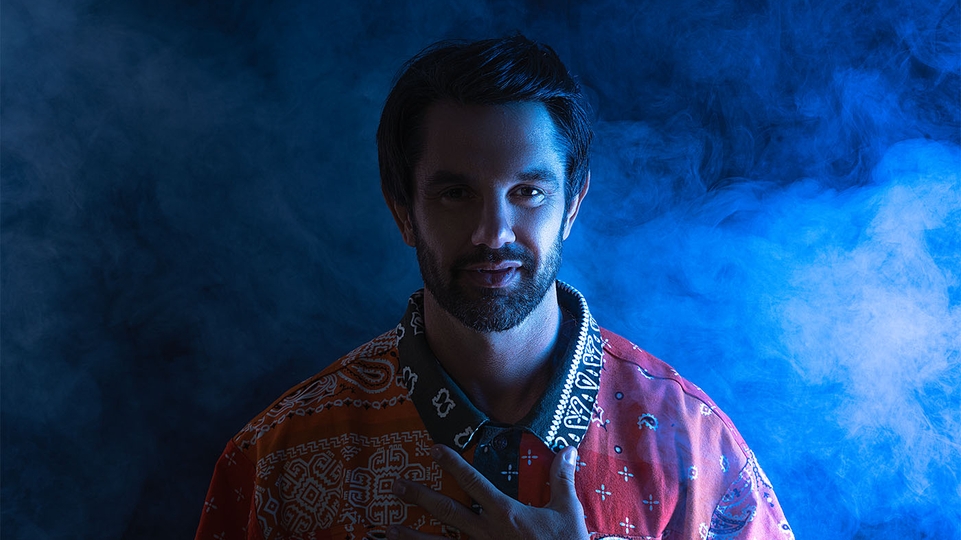 Soldera standing in a red patterned shirt amidst blue-lit smoke