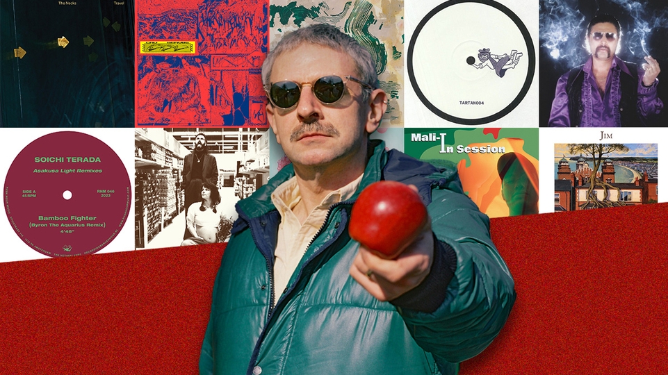 Ruf Dug in a green puffer jacket and sunglasses holding an apple in front of him, standing in front of a selection of artwork from his Selections