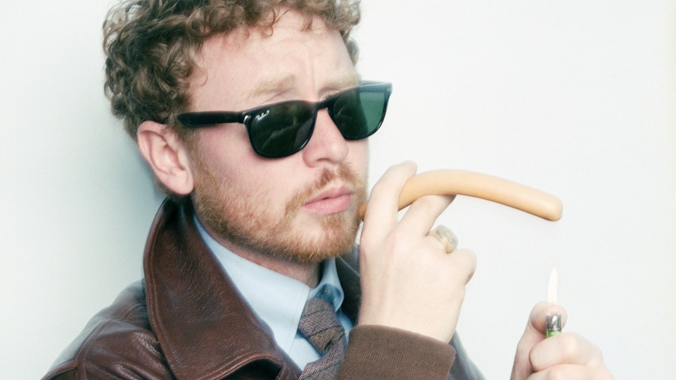 Photo of Julio Bashmore wearing black glasses and pretending to smoke a hot dog