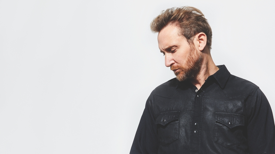 Photo of David Guetta posing sideways in front of a white background.