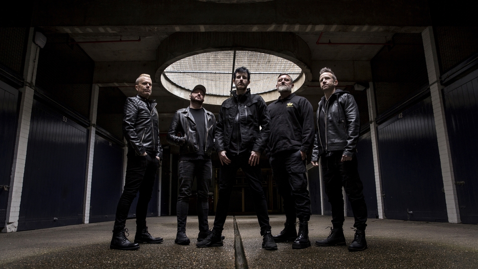 Photo of the five members of Pendulum standing in an industrial space.