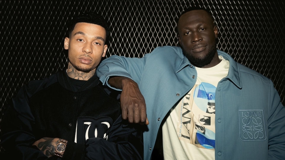 Photo of Stormzy wearing a blue jacket and resting his arm on Fredo’s shoulder