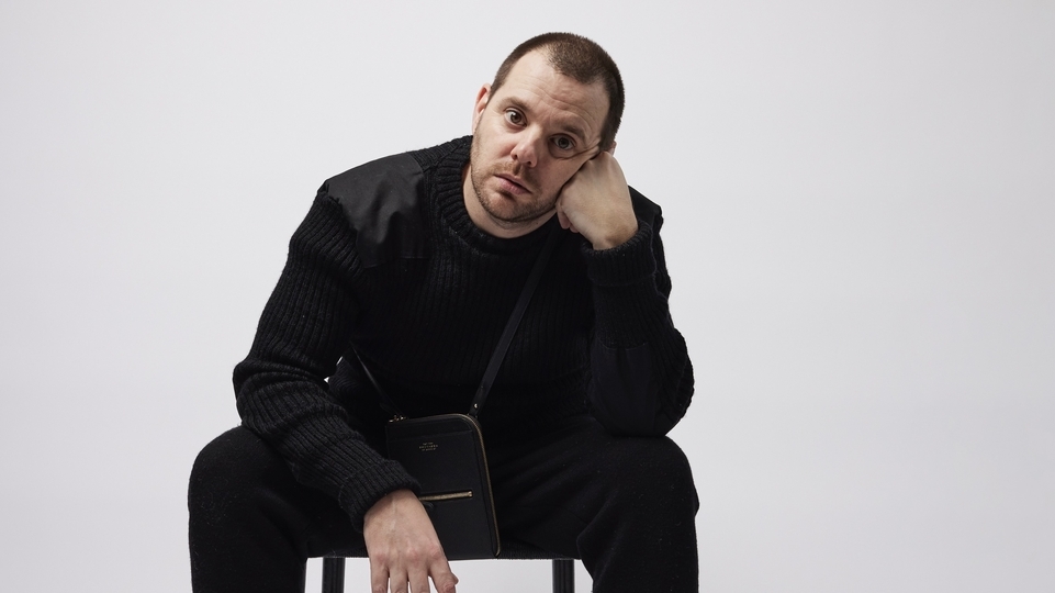 Photo of The Streets’ Mike Skinner sitting on a chair and wearing all black