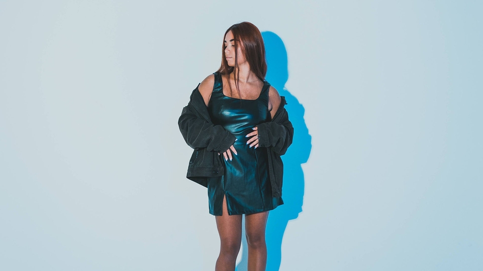 Sabrina standing in a dark blue dress with a black denim jacket off her shoulders