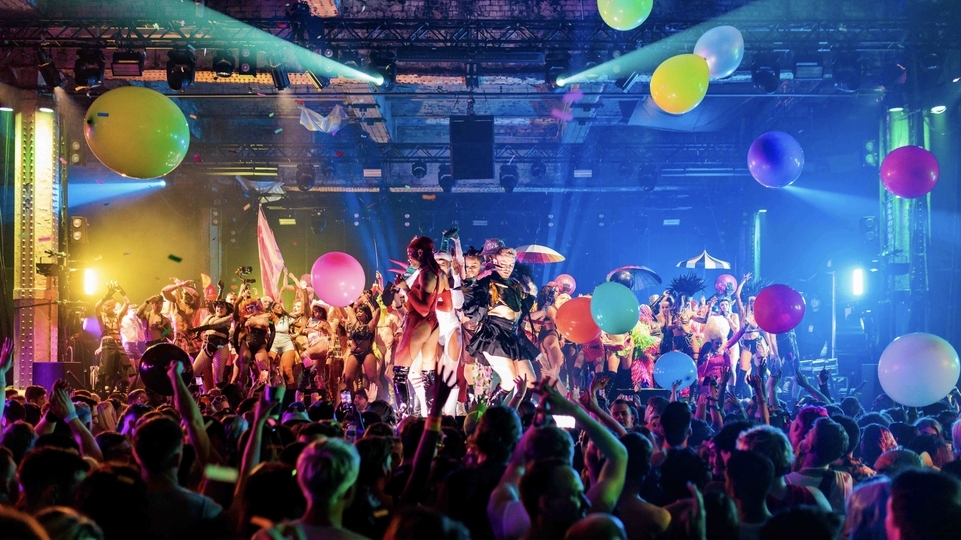 Photo of dancers on stage at Homobloc festival with colourful lights, balloons, and a busy crowd