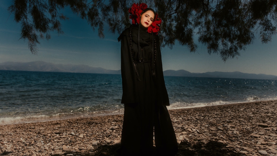Photo of Sofia Kourtesis standing on a beach wearing a black gown