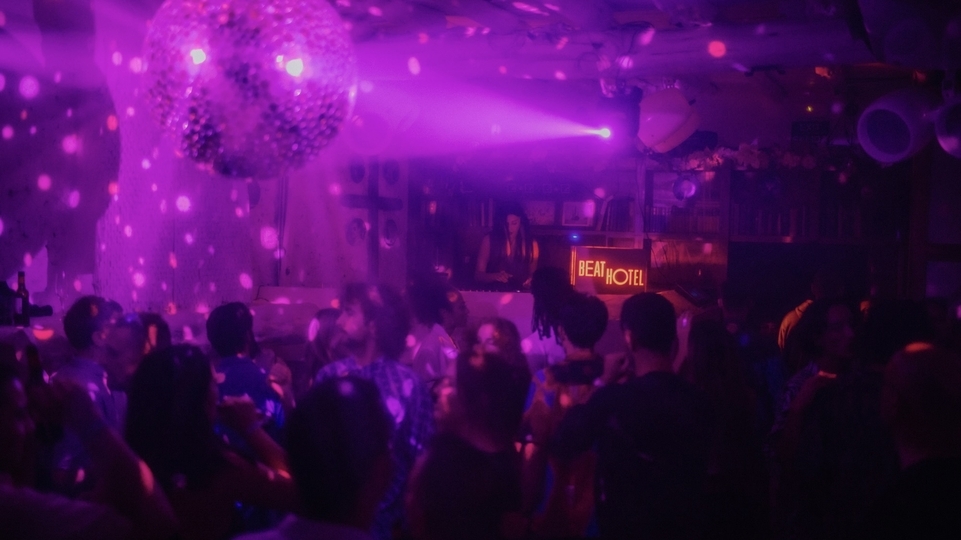 Photo of a purple-lit dancefloor with a disco ball and neon ‘beat hotel’ sign